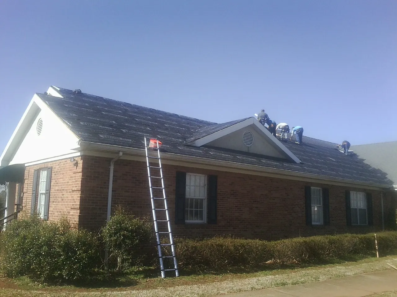 Crew tearing shingles off a brick ranch roof with a ladder set — Metal Roof Repair work by our crew in Moores Hill