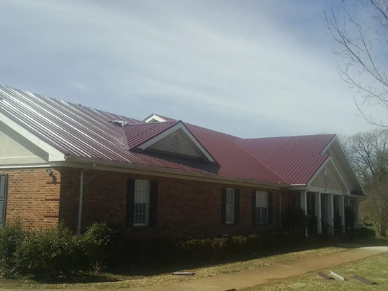 Red metal roof with gabled entries on a long brick building, from a Hail Damage Roof Repair job in Moores Hill