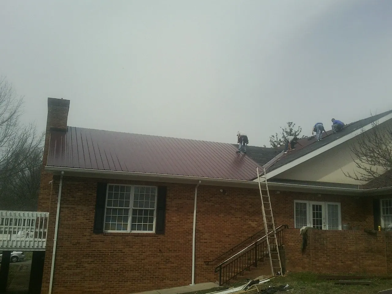 Crew setting red metal roofing panels on a brick home in Moores Hill