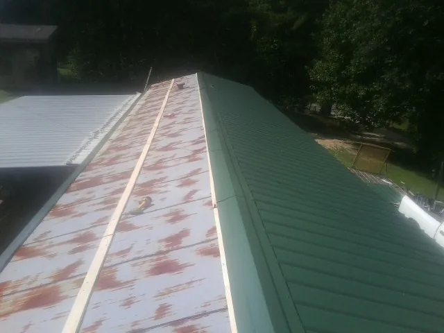 Old rusted panels beside newly installed green metal roofing — Wind Damage Roof Repair by Roofing Brothers in Moores Hill