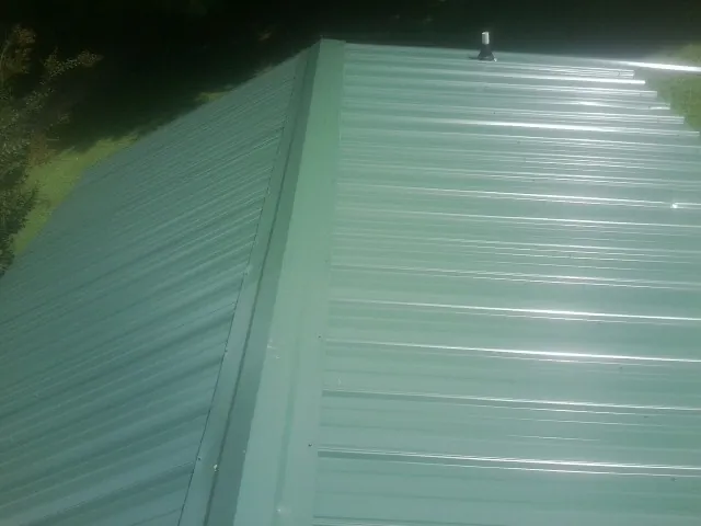 New green metal panels meeting at the ridge of a roof — Flat Roof Repair work by our crew in Moores Hill