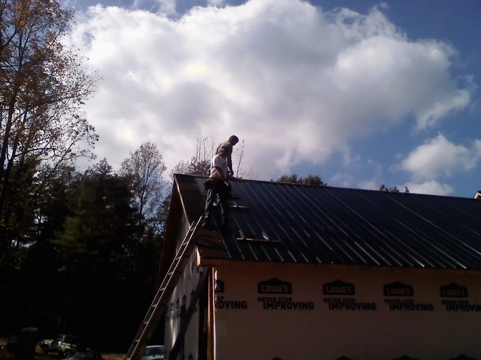 Roofer fastening dark metal panels high against a cloudy sky, from a Roof Inspection job in Moores Hill
