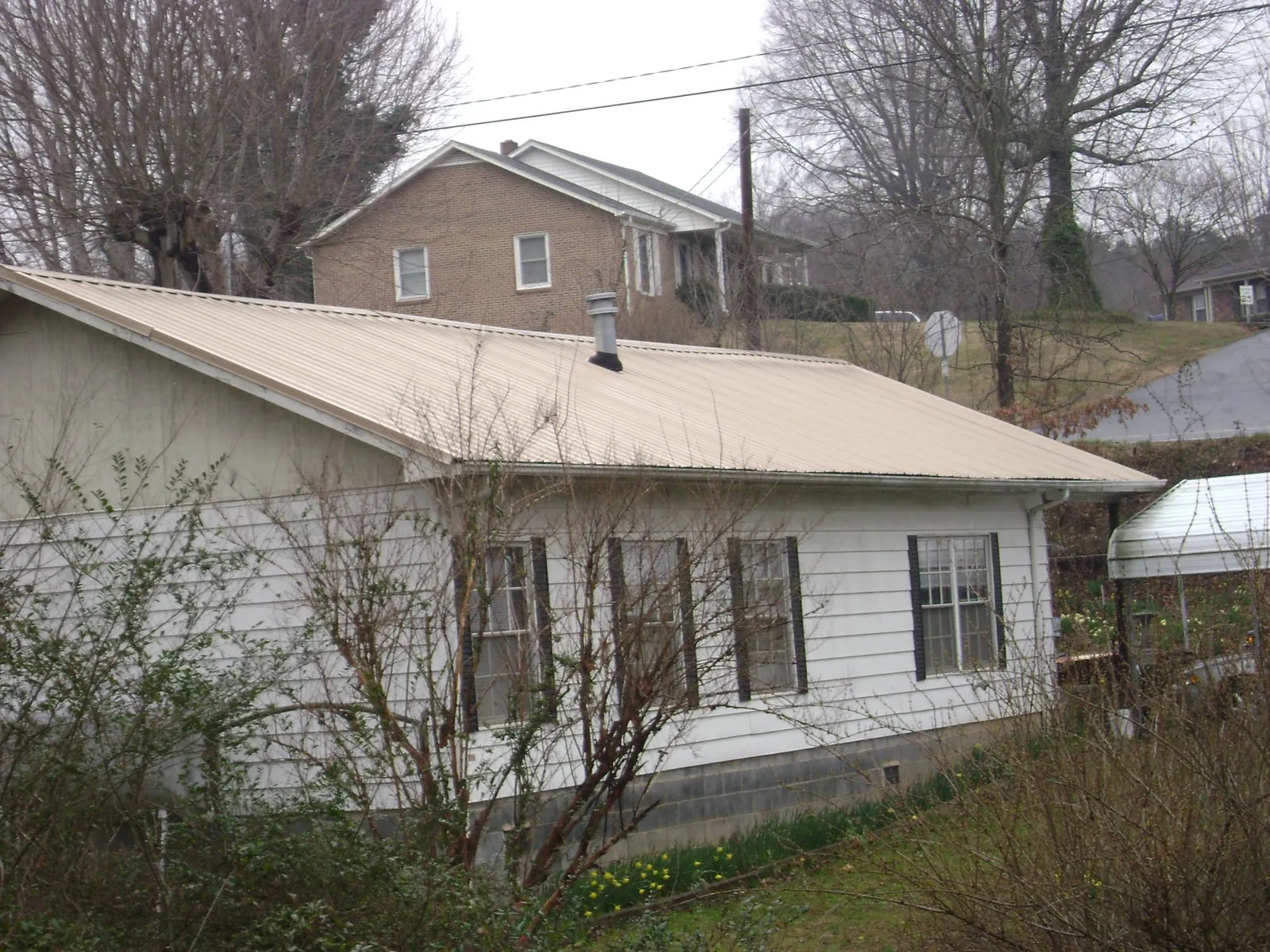 Tan metal roof on a white sided house set into a hillside — Commercial Roofing by Roofing Brothers in Moores Hill