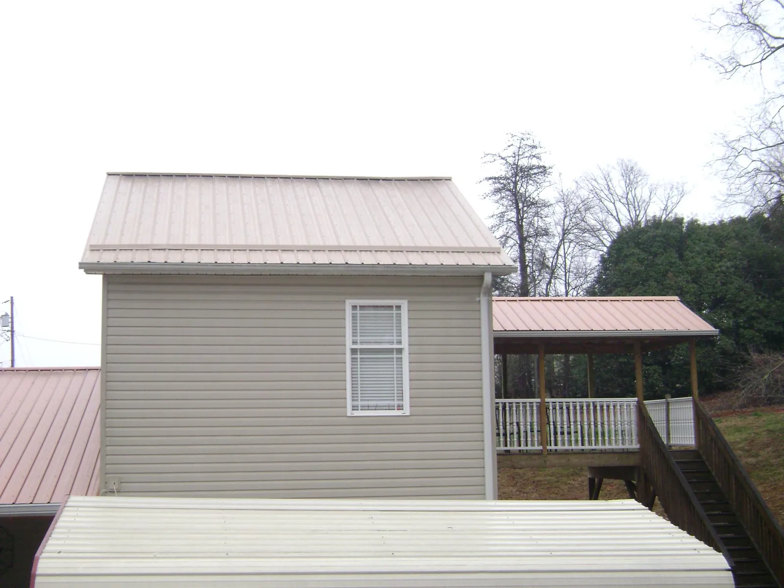 Tan metal roofs on a two story addition and attached porch, from a Roof Replacement job in Moores Hill